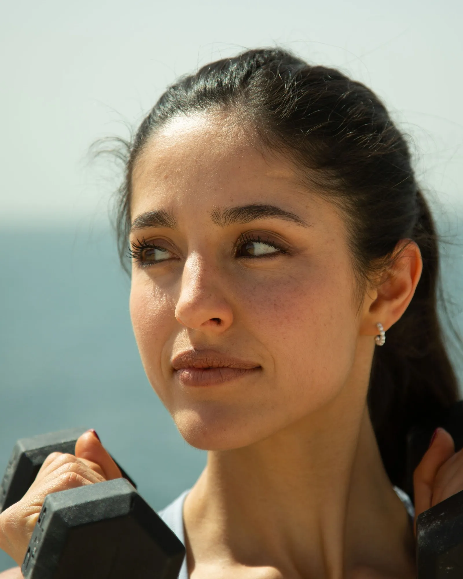 Anna Falchi holding two dumbbells at shoulder height, by the sea