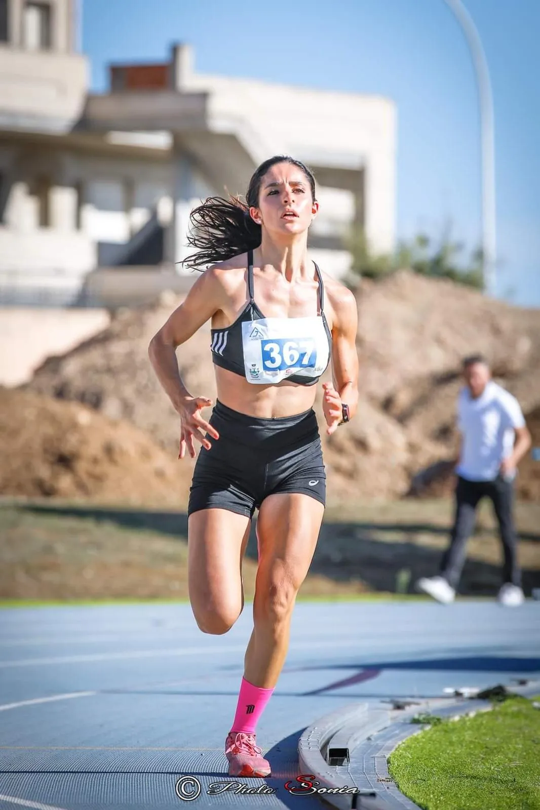 Anna che corre con il pettorale durante una gara trail, concentrata, in una giornata di sole
